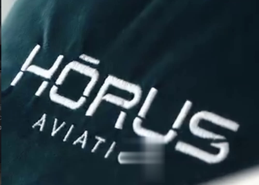 Tapete verde bordado com o logo Hōrus Aviation na entrada da aeronave